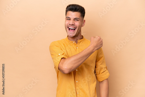 Young caucasian man isolated on beige background celebrating a victory
