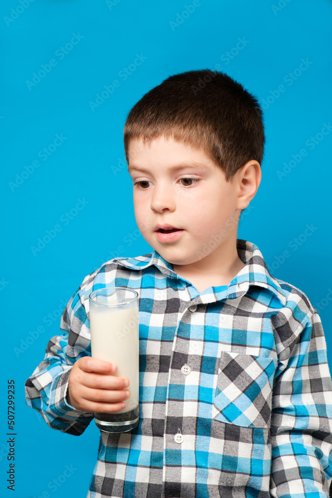 A 4 year old boy holds a glass of milk and looks to the side, vertical photo, copy the place for text A 4 year old boy holds a glass of milk and looks to the side, vertical photo, copy the place for text