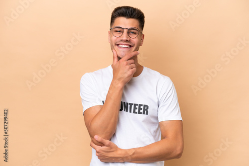 Young volunteer caucasian man isolated on beige background smiling