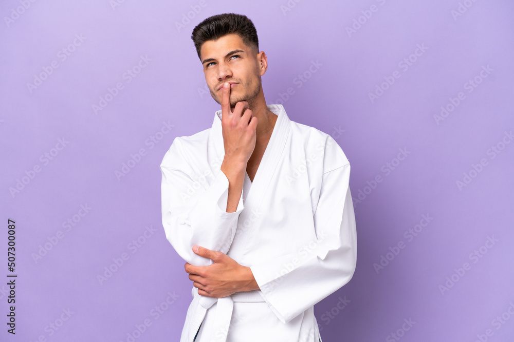 Young caucasian man doing karate isolated on purple background having doubts while looking up Young caucasian man doing karate isolated on purple background having doubts while looking up