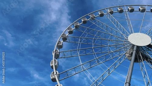 A tall Ferris wheel with closed booths slowly rises against the blue sky. High quality 4k footage photo