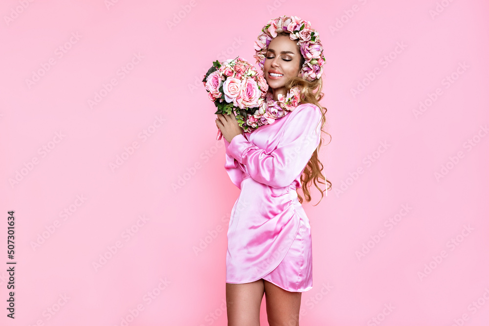 Spring fashion model. Beautiful natural woman is wearing pink dress and wreath with flowers. Elegant woman is holding bouquet on pink background. Studio shoot. Spring fashion model. Beautiful natural woman is wearing pink dress and wreath with flowers. Elegant woman is holding bouquet on pink background. Studio shoot.