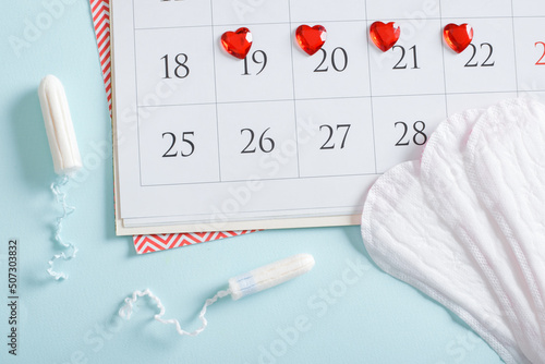 Calendar of the female menstrual cycle with pads and tampons on a light blue background.