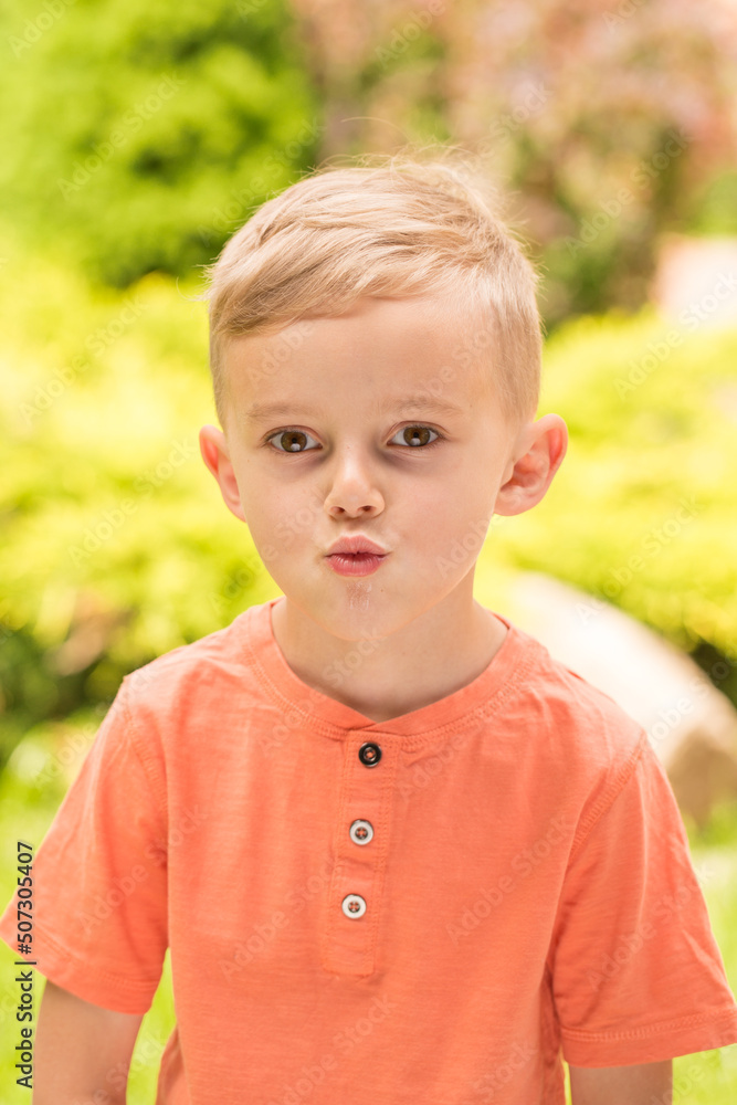 five-year-old boy making faces. A five-year-old blond boy makes faces while standing on the street in sunny weather five-year-old boy making faces. A five-year-old blond boy makes faces while standing on the street in sunny weather