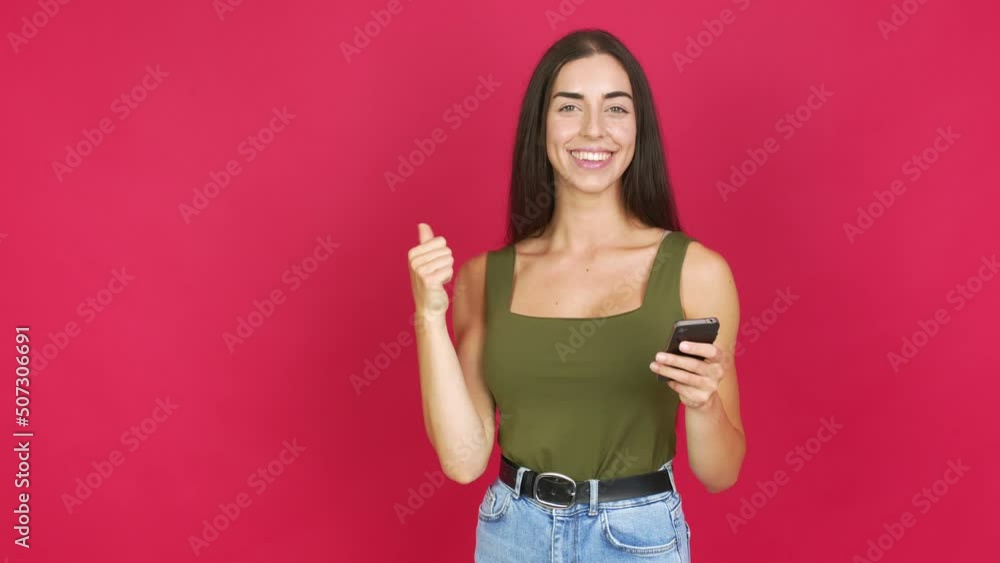 Young brunette woman using mobile phone and pointing side over isolated background Young brunette woman using mobile phone and pointing side over isolated background