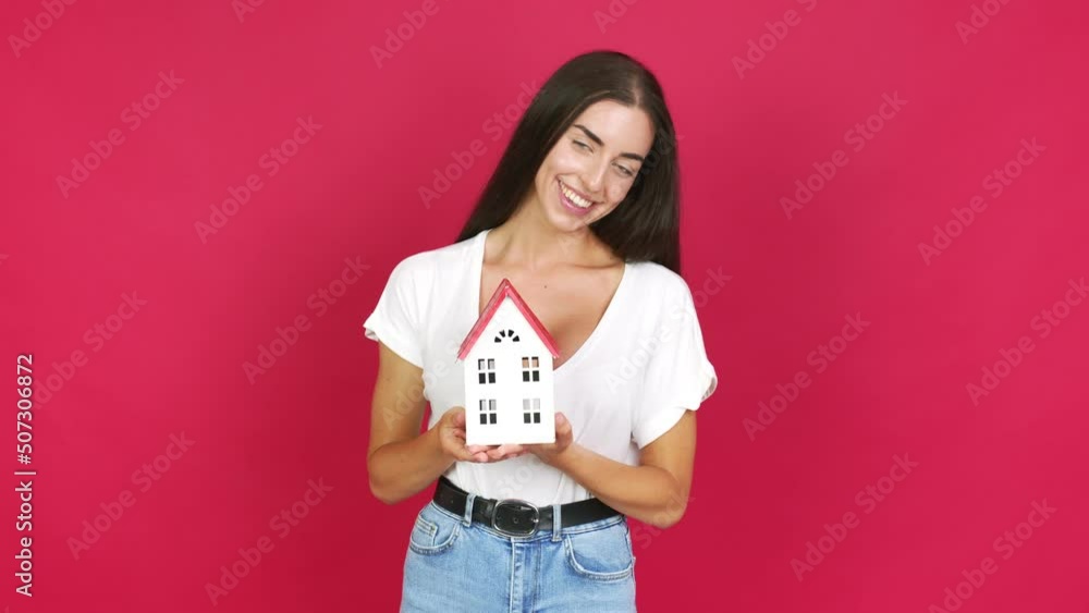 Young brunette woman holding a little house over isolated background Young brunette woman holding a little house over isolated background