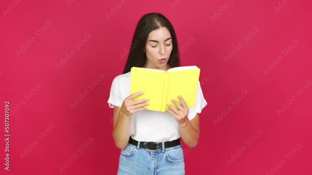 Young brunette woman surprised and holding a book over isolated background Young brunette woman surprised and holding a book over isolated background
