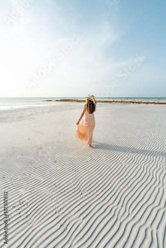 young hispanic woman with dress and hat on a beach with textured sand