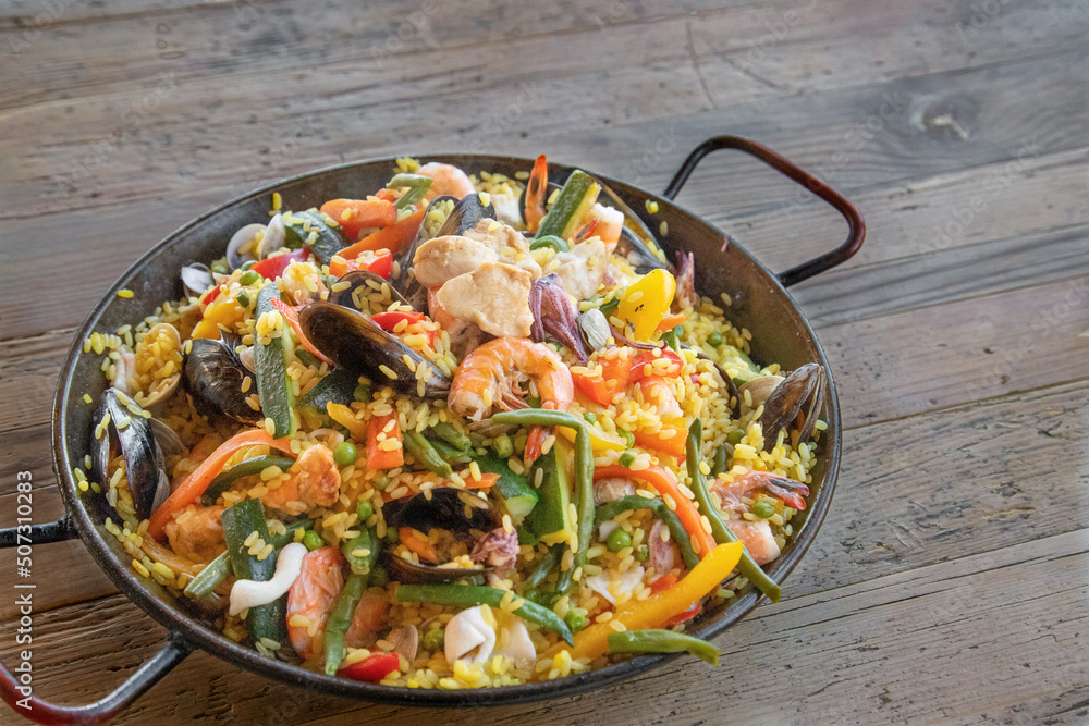 Paella Valenciana, typical spanish food with rice, fish and vegetables - wooden table Paella Valenciana, typical spanish food with rice, fish and vegetables - wooden table