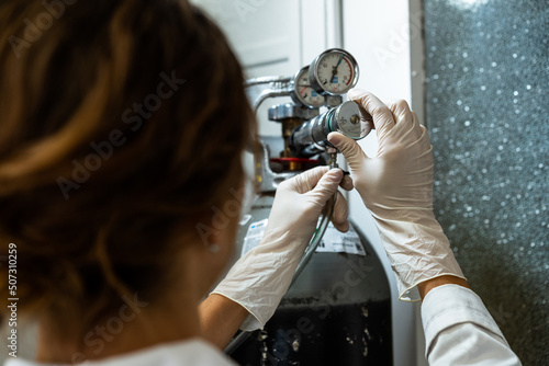 Female technician in gloves adjusting a barometer of a nitrogen cylinder or compressed air