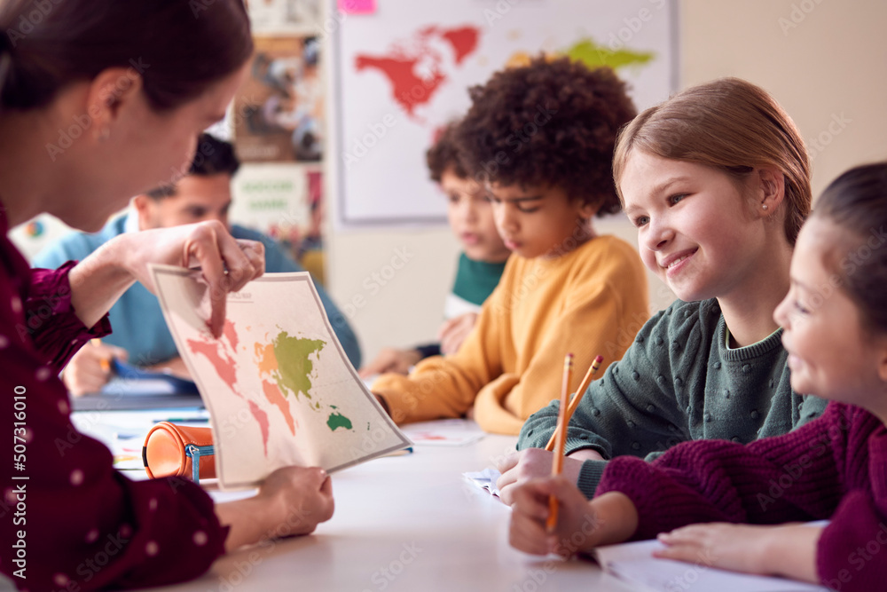 Group Of Multi-Cultural Students With Teachers In Classroom Looking At Map In Geography Lesson Group Of Multi-Cultural Students With Teachers In Classroom Looking At Map In Geography Lesson