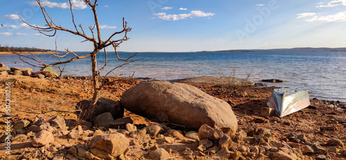Linda vista da marchem da represa de três marias, com água límpida, céu azul com nuvens e uma lancha logo a frente de grande pedra, na região de Três Marias, Minas Gerais, Brasil.