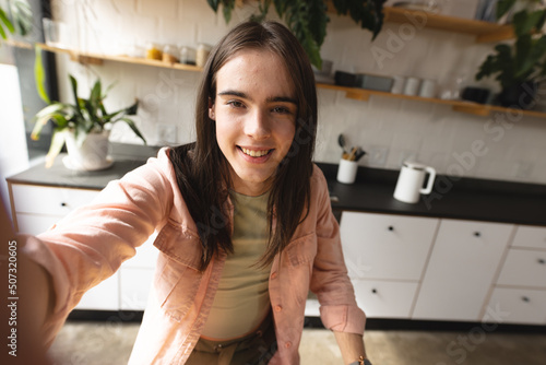 Portrait of non-binary trans woman smiling looking at the camera in the kitchen at home photo