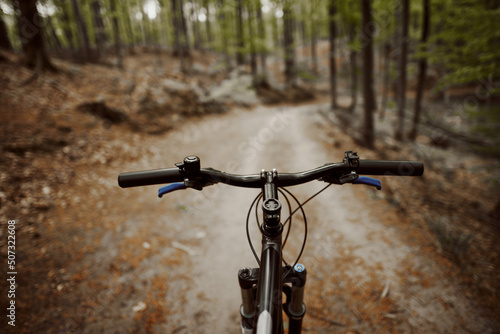 Mountain bike handlebar viewed from the first-person perspective. visible bicycle frame and bicycle accessories on the handlebar and the forest trai. Concept of spending time outdoors while bikeriding photo