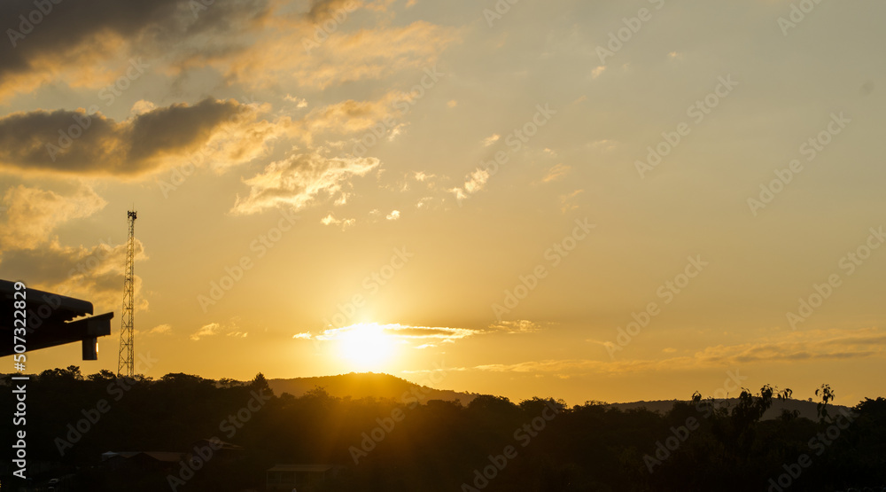 Pôr do sol entre montanhas, torres e céu limpo com nuvens, visto em sítio localizado em Juatuba, Minas Gerais, Brasil.