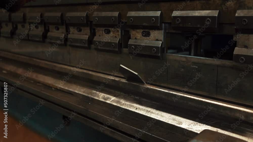Man working with sheet metal on CNC hydraulic press brake. He puts the part and bends it into a large machine at an angle Man working with sheet metal on CNC hydraulic press brake. He puts the part and bends it into a large machine at an angle