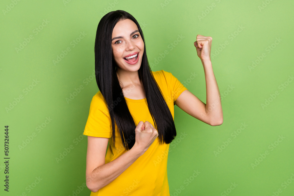 Photo of pretty lucky lady dressed yellow t-shirt rising fists smiling isolated green color background Photo of pretty lucky lady dressed yellow t-shirt rising fists smiling isolated green color background