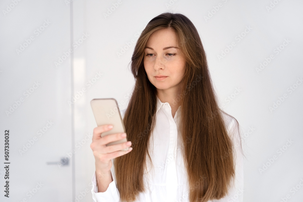 Pretty young caucasian brunette woman with long brown hair using mobile phone,reading or texting messages indoors on white background. Half-length shot,copy space Pretty young caucasian brunette woman with long brown hair using mobile phone,reading or texting messages indoors on white background. Half-length shot,copy space