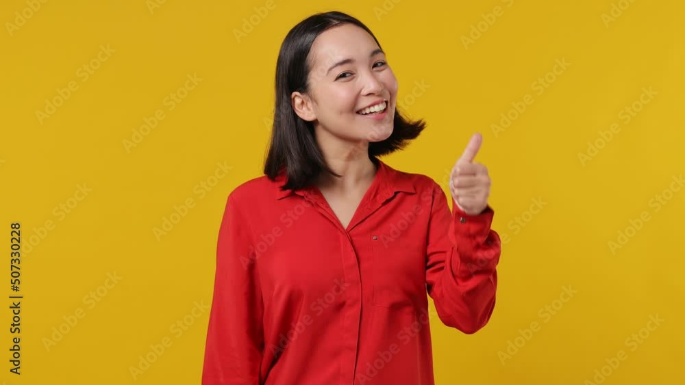 Excited cheerful fancy young woman of Asian ethnicity 20s years old wears red shirt showing thumb up like gesture isolated on plain yellow background studio portrait. People emotions lifestyle concept Excited cheerful fancy young woman of Asian ethnicity 20s years old wears red shirt showing thumb up like gesture isolated on plain yellow background studio portrait. People emotions lifestyle concept