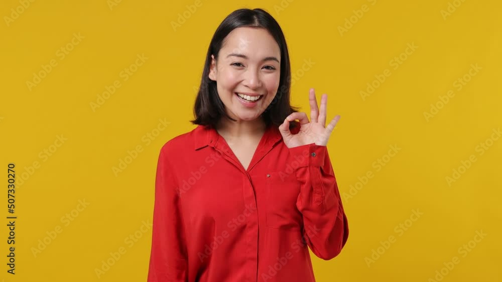 Smiling cheerful young woman of Asian ethnicity 20s years old wear red shirt showing okay ok zero fingers gesture isolated on plain yellow background studio portrait. People emotions lifestyle concept Smiling cheerful young woman of Asian ethnicity 20s years old wear red shirt showing okay ok zero fingers gesture isolated on plain yellow background studio portrait. People emotions lifestyle concept