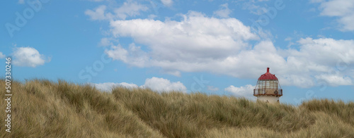 the red top and light of the point of ayr lighthouse peeking over the marram covered sand dunes at talacre beach photo