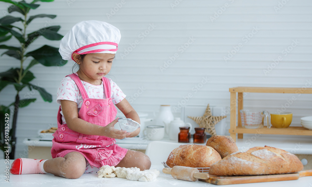 Cute little chef sitting on the table learning to make bread Cute little chef sitting on the table learning to make bread