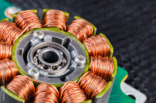 Electric engine stator with coils copper wire winding or ball bearing on green PCB detail. Closeup of step motor inductors or metal ferromagnetic sheets from laser printer machine on blurry black net.