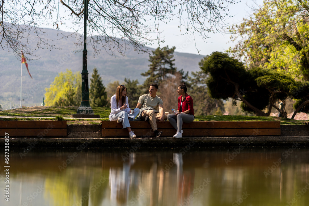 Three happy friends talking taking a conversation near water Three happy friends talking taking a conversation near water