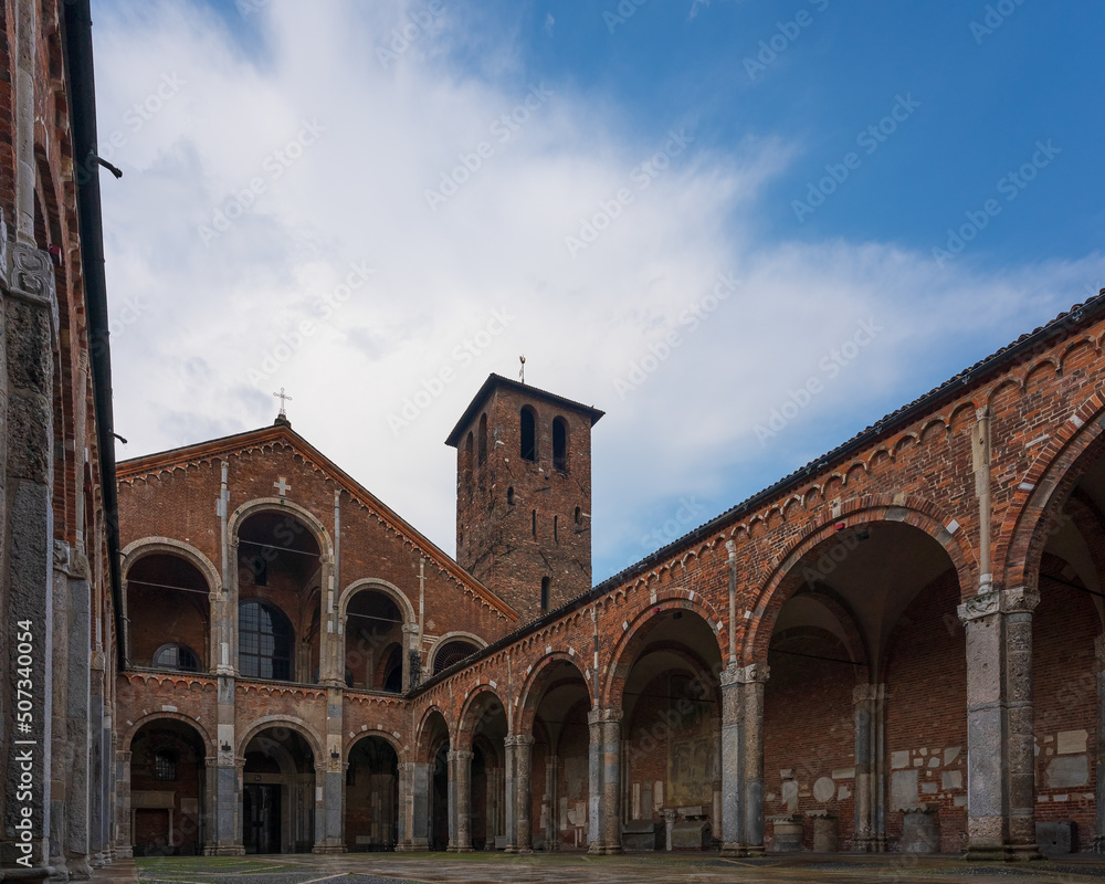 Saint Ambrogio church brick building with bell towers, courtyard, arches at overcast day, Milan, Lombardy, Italy