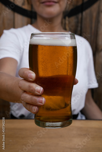 Closeup view of a young woman holding a glass of golden beer in the bar. 