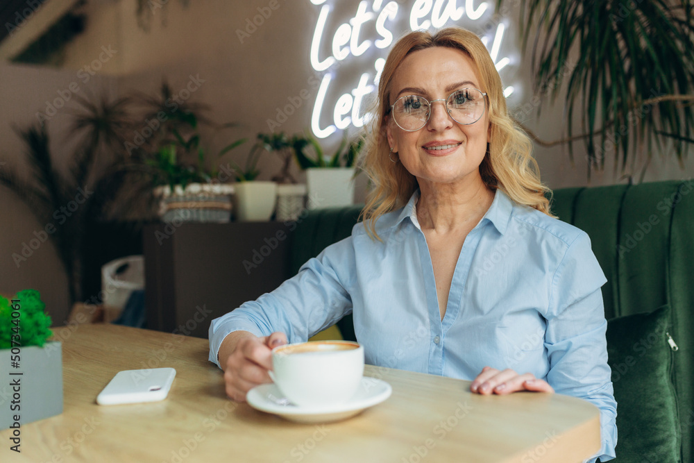 Beautiful smiling woman drinking coffee at cafe. Portrait of mature woman in a cafeteria drinking hot cappuccino wear stylish clothes Pretty woman with cup of coffee Beautiful smiling woman drinking coffee at cafe. Portrait of mature woman in a cafeteria drinking hot cappuccino wear stylish clothes Pretty woman with cup of coffee