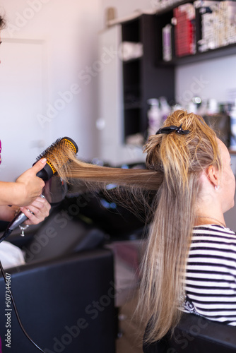 Drying hair with hair dryer and round brush at hairdresser. Selective focus.
