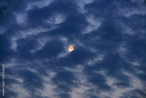 Full moon partly covered with altocumulus clouds, just before the sunrise, almost dawn