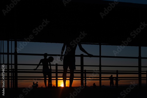 silhouette of two young people playing soccer on a port walkway on a beach in Portugal at sunset