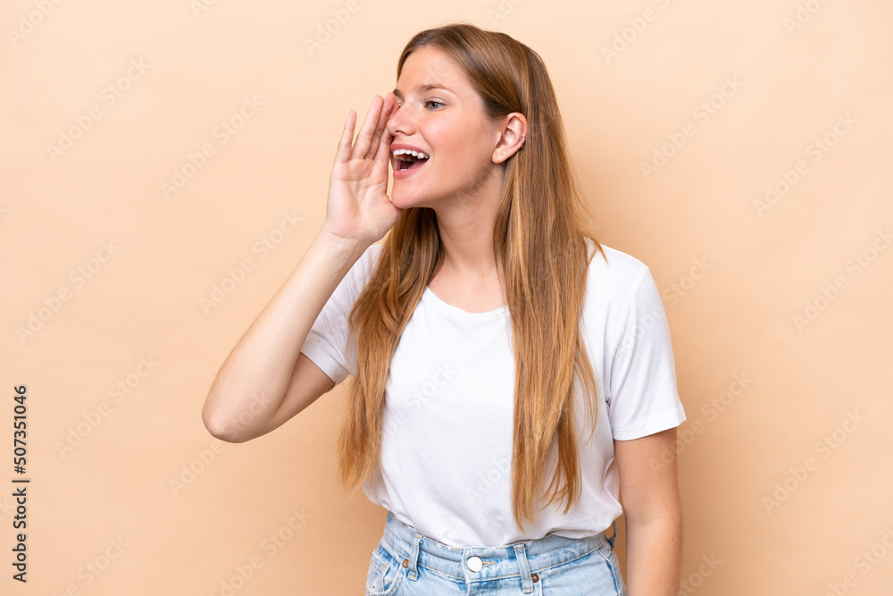 Young caucasian woman isolated on beige background shouting with mouth wide open to the side Young caucasian woman isolated on beige background shouting with mouth wide open to the side