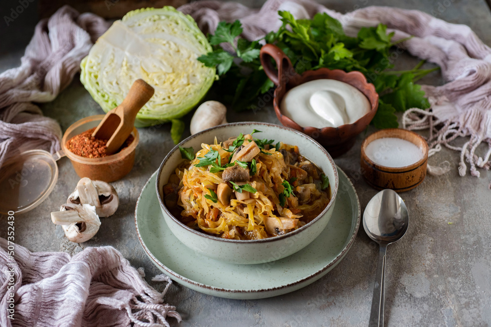 A hearty lunch for the whole family: cabbage stewed with vegetables and mushrooms in a beautiful place on a gray background. Close-up