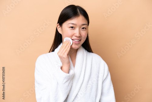 Quadro em tela Young Chinese woman isolated on beige background with cotton pad for removing ma