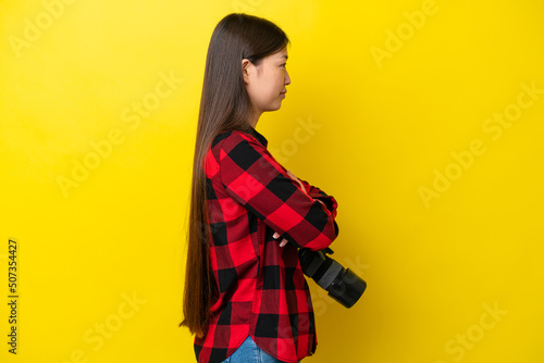 Young photographer Chinese woman isolated on yellow background in lateral position © luismolinero