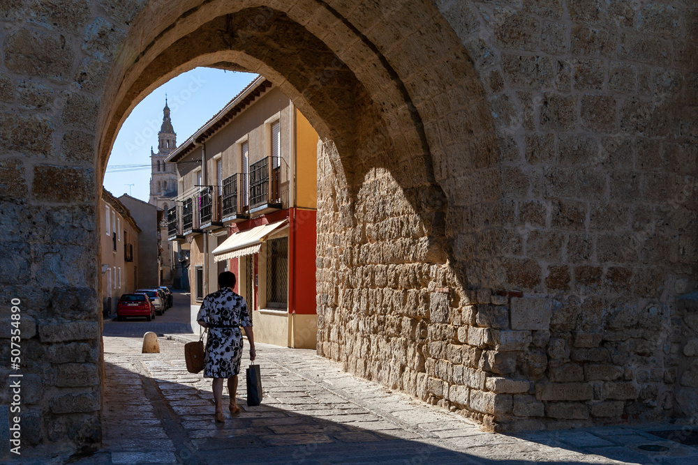 an elderly woman strolls through a small, uninhabited Spanish village  
