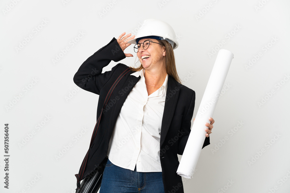 Middle age architect woman with helmet and holding blueprints over isolated background smiling a lot Middle age architect woman with helmet and holding blueprints over isolated background smiling a lot