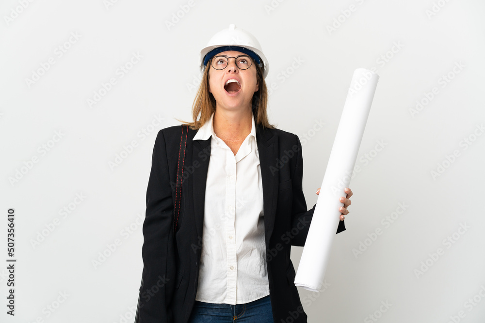 Middle age architect woman with helmet and holding blueprints over isolated background looking up and with surprised expression Middle age architect woman with helmet and holding blueprints over isolated background looking up and with surprised expression