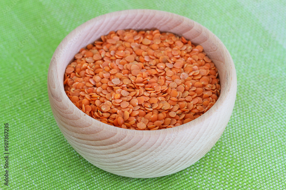 Uncooked red lentils in wooden bowl on green background