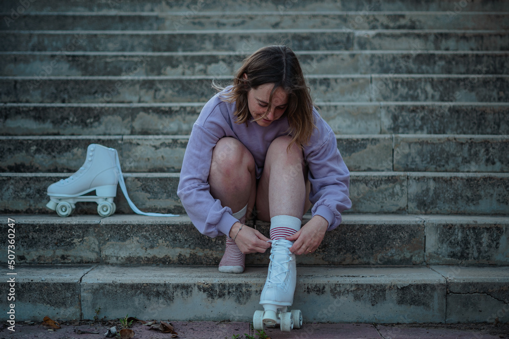 Young woman tying the laces of her roller skates while sitting on stairs