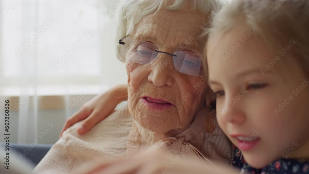 Close up shot of little girl reading book together with elderly grandmother at home Close up shot of little girl reading book together with elderly grandmother at home