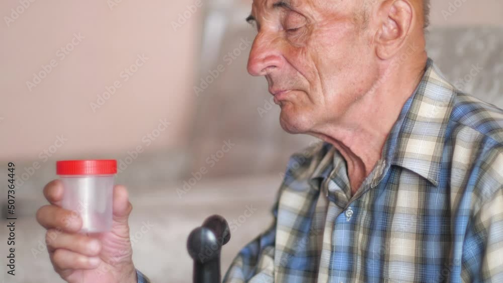 doctor in a medical glove gives a container for analysis to an elderly caucasian patient 70-79 years old. A pensioner aged with dementia holds a walking stick. Mental health doctor in a medical glove gives a container for analysis to an elderly caucasian patient 70-79 years old. A pensioner aged with dementia holds a walking stick. Mental health