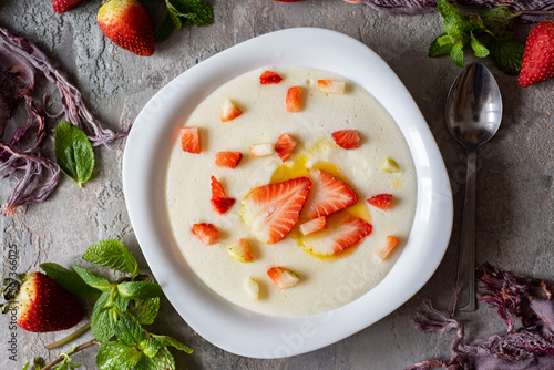 Breakfast for children: milk semolina porridge with strawberries on a white plate on a gray background. Semolina porridge with milk for lunch. View from above.