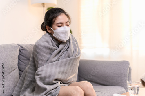 Young Asian woman wearing face mask have a cold and high fever have to rest at her home and absent from her job. Daily lifestyle health care concept.