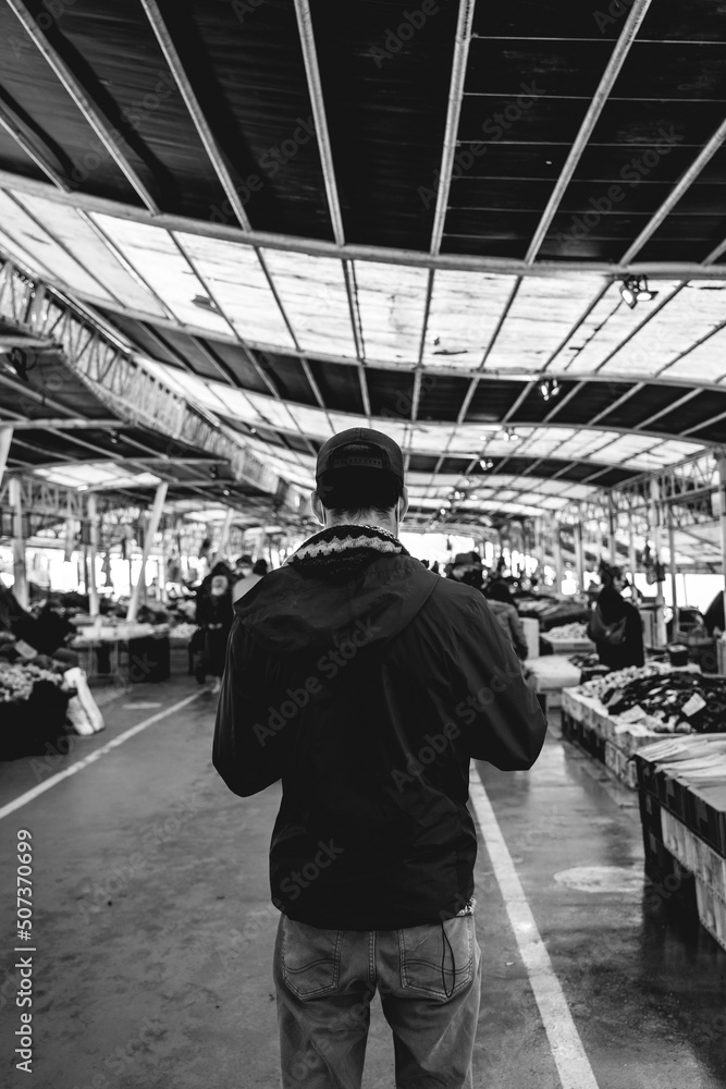 Young guy with jacket and cap from behind in the public 'Mercado Fluvial' (river market), Valdivia, Chile (in black and white) Young guy with jacket and cap from behind in the public 'Mercado Fluvial' (river market), Valdivia, Chile (in black and white)