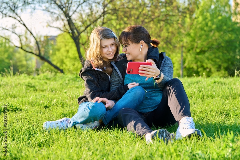 Mom and daughter looking together at smartphone screen, outdoor