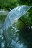 transparent umbrella in water drops in puddle on road, natural abstract green background. symbol of rainy season, bad wet stormy weather. melancholy mood